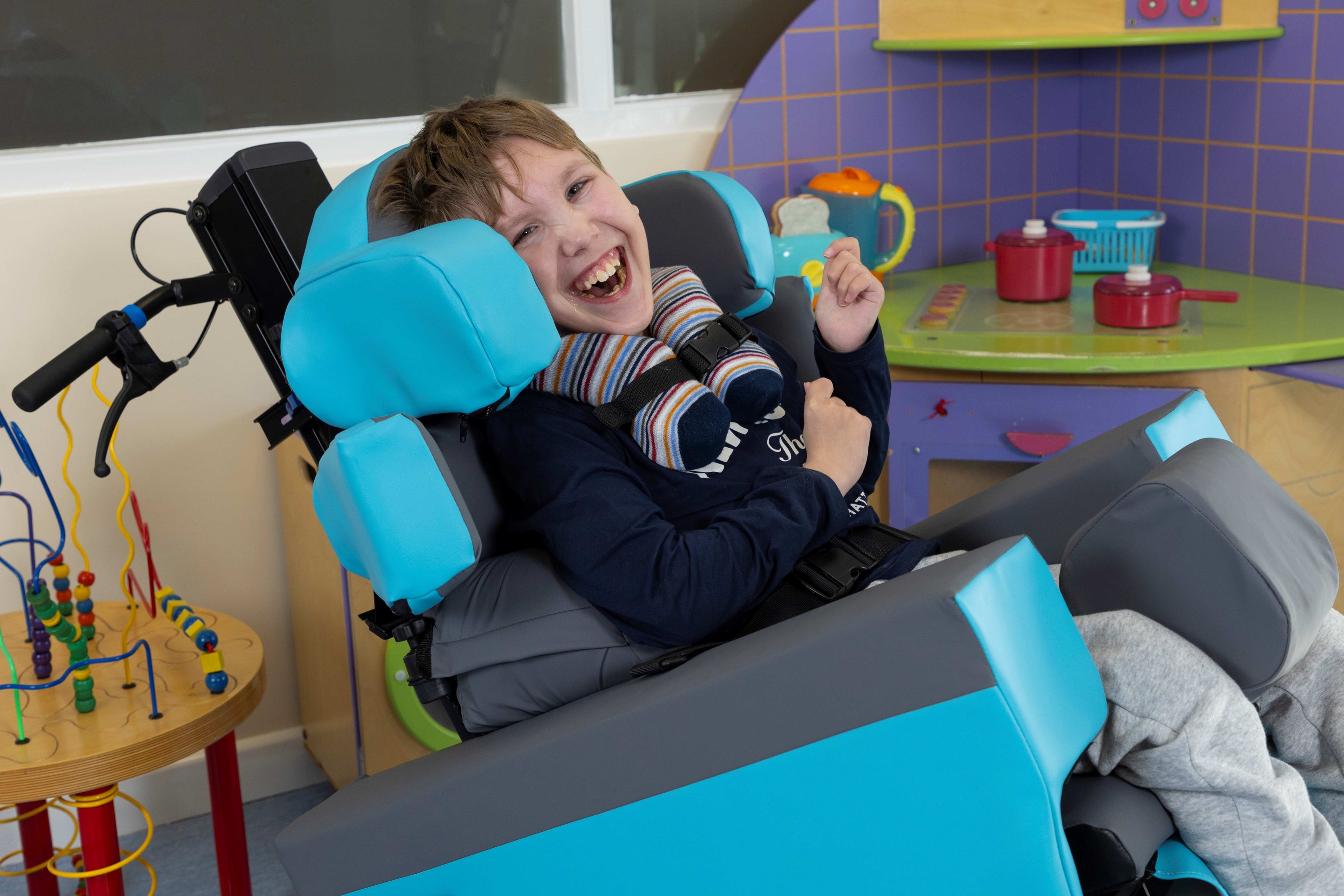 Child in a CareFlex Specialist Seating Chair with blue headrests in a colorful room